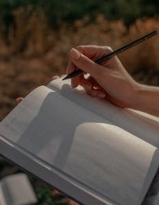 Close-up of a woman writing in a journal outdoors on a sunny day.